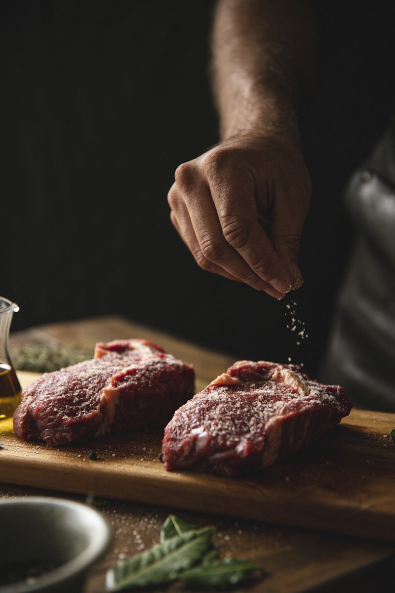 Raw steak being generously seasoned with salt and pepper